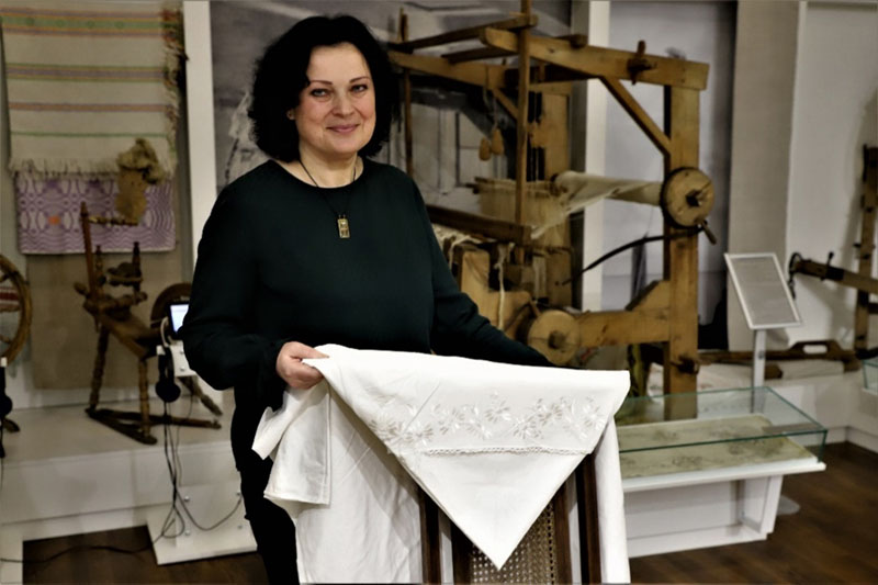 Irena Ungaro su savo močiutės Annos Wiethe šilku siuvinėtu patalų užvalkalu. MLIM ekspozicija, 2022 m.