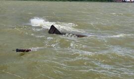 Į krantą traukiamas apvirtęs laivas kurėnas